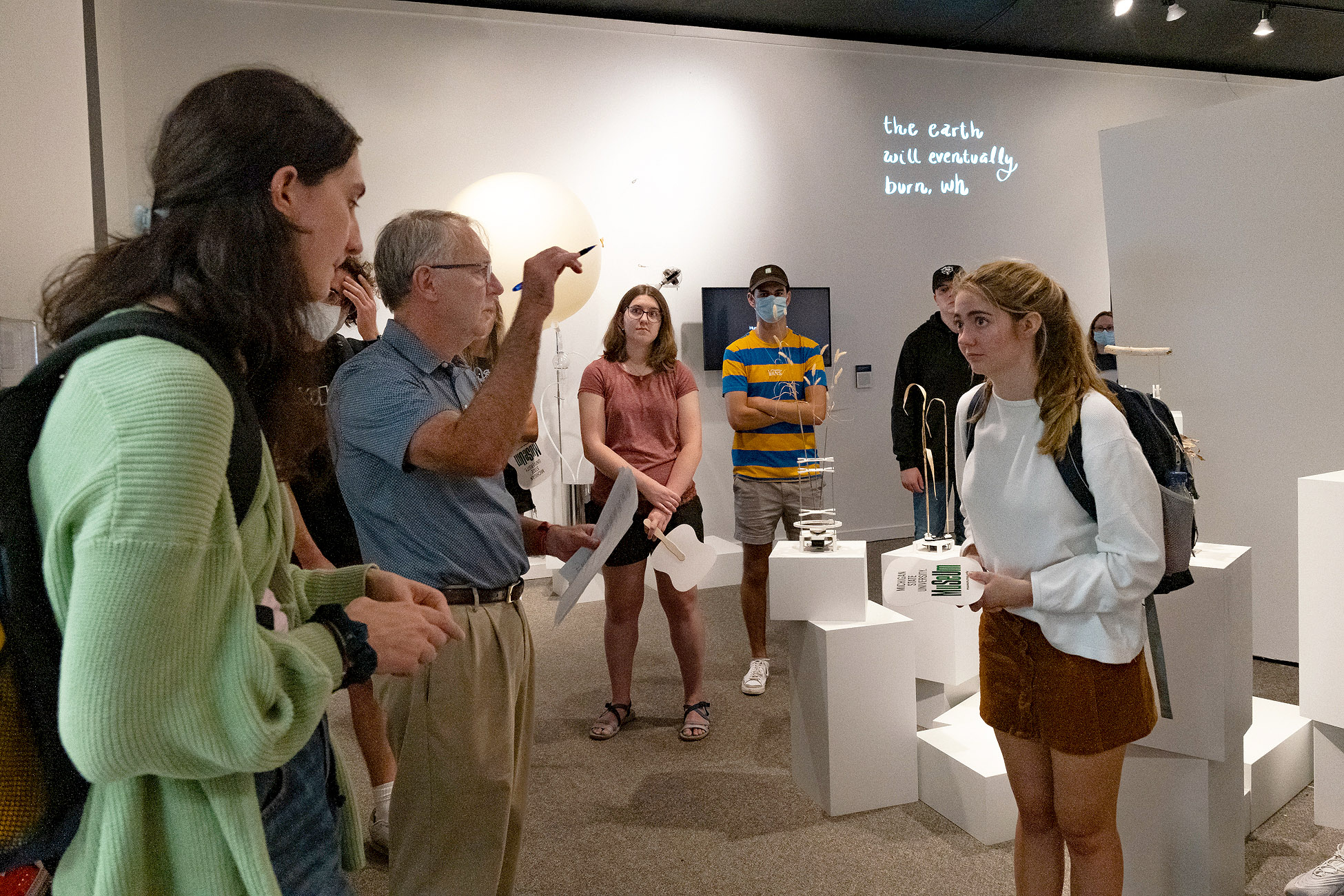 Image of people standing and gathered in the Museum, listening to an instructor.