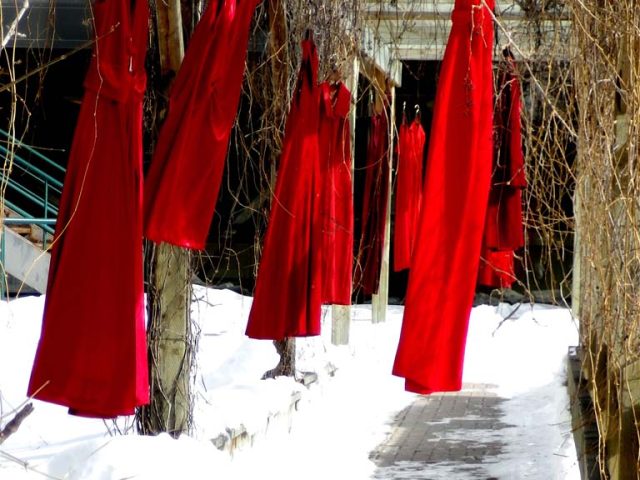 Several long, bright red dresses hang outdoors on a snowy day, spotlighting the crisis of missing and murdered Indigenous women and girls.