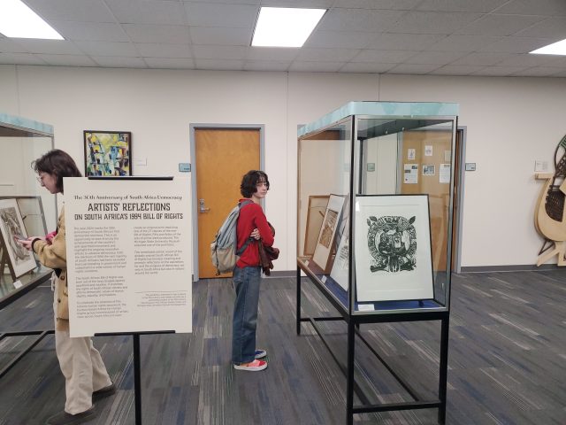 Two MSU students stand in front of a glass case holding one of the South African prints from MSU Museum's collections.