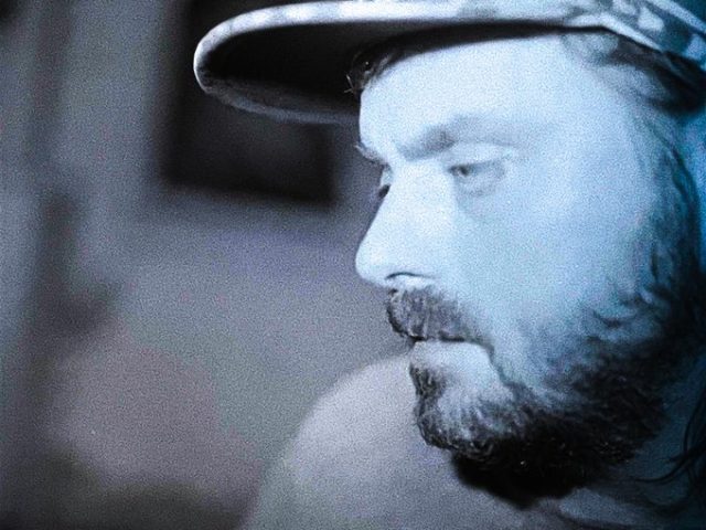 A Blue toned profile portrait of Abel Korinsky wearing a baseball hat.