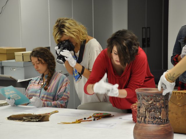 A group of MSU graduate students examine collections sat out on a white table, each wearing white gloves and one with a camera.