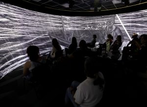 Participants in the Immersive Visualization Institute look at a black and white woodcut image projected in the 360-degree room in the Digital Scholarship Lab at the main MSU Library.