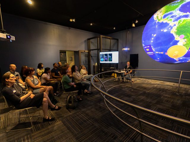 Participants in the Immersive Visualization Institute look at a map of the world projected onto a 6-foot globe in the Science on a Sphere Gallery at the MSU Museum.