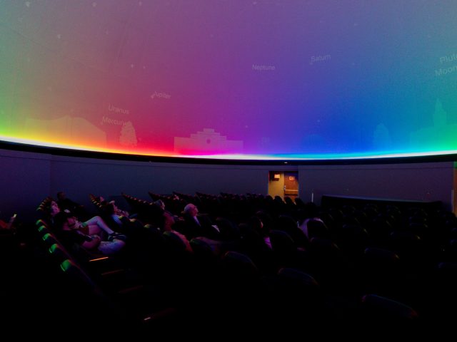 Participants in the Immersive Visualization Institute look up at a colorful image on the dome of the Abrams Planetarium.