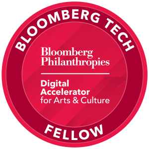 Round badge in shades of red with white text that reads 'Bloomberg Tech Fellow' around the top edge and 'Bloomberg Philanthropies Digital Accelerator for Arts & Culture' in the center.