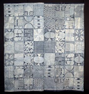 Rectangular textile composed of multiple square panels, each featuring unique indigo and white geometric or abstract patterns, including grids, spirals, ovals, and stylized motifs.